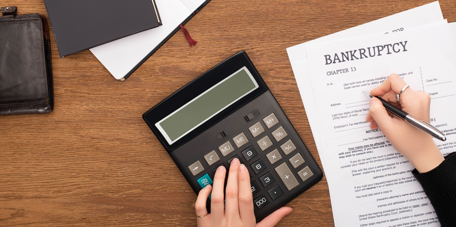 partial view of woman filling in bankruptcy form and using calculator on wooden background