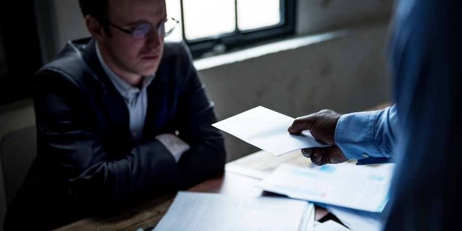 a man in a suit sitting at a desk is handed a piece of paper