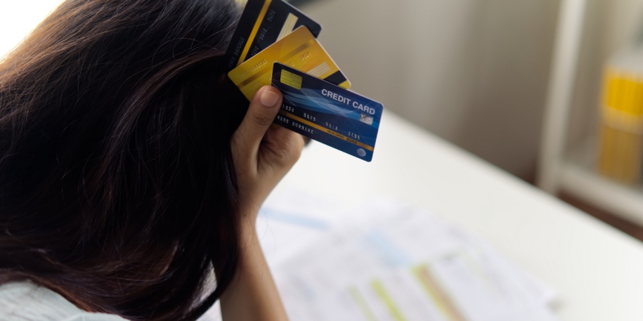 a woman holds her forehead with 3 credit cards in hand